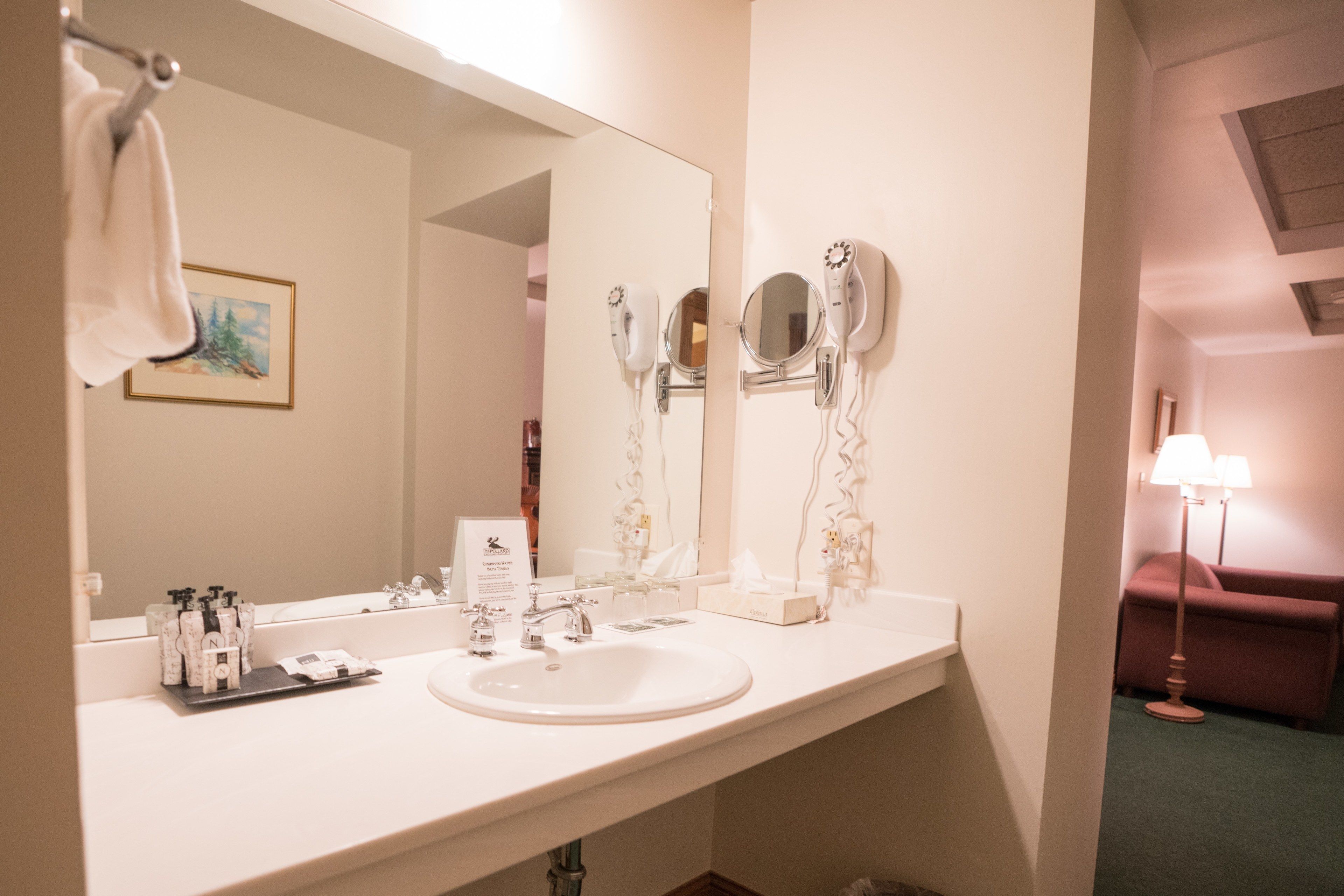 Un baño de hotel con un espejo grande, dos secadores de pelo, un lavabo y un perchero para toallas.