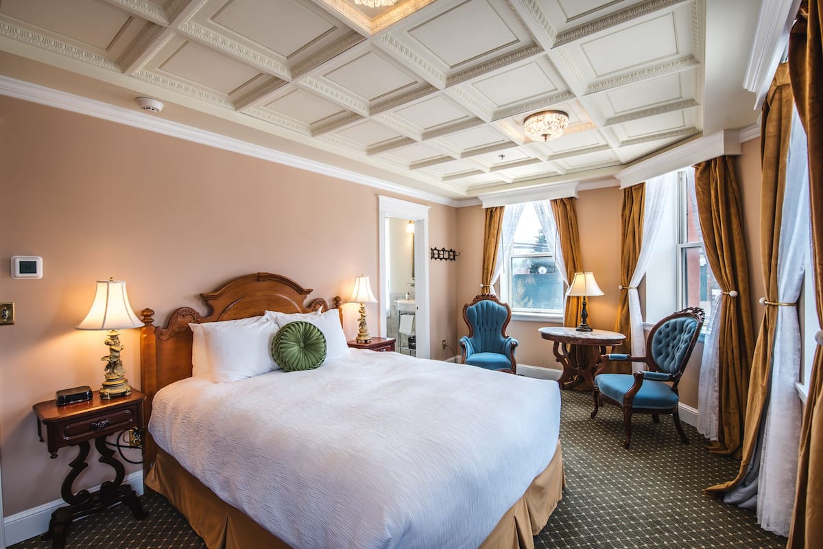 Habitación de hotel con una cama grande, un escritorio, una silla y una ventana con cortinas.