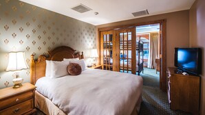 A hotel room with a large bed, wooden headboard, a television, and a view of the outside through a glass door.