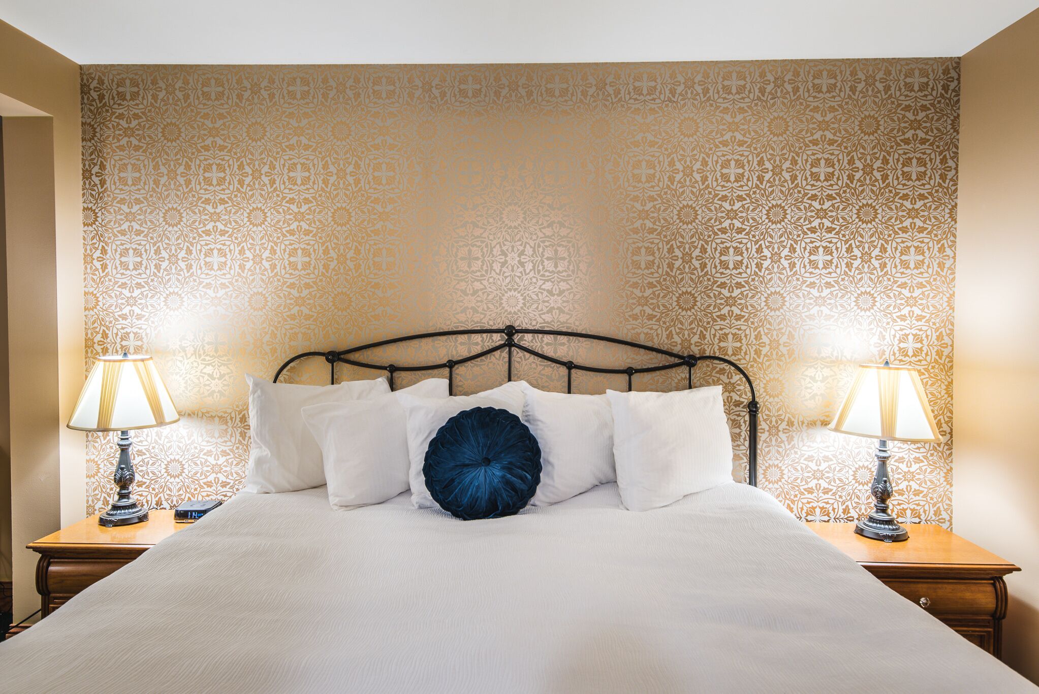 A neatly made bed with white linens, a dark blue decorative pillow, and two bedside lamps on wooden nightstands.