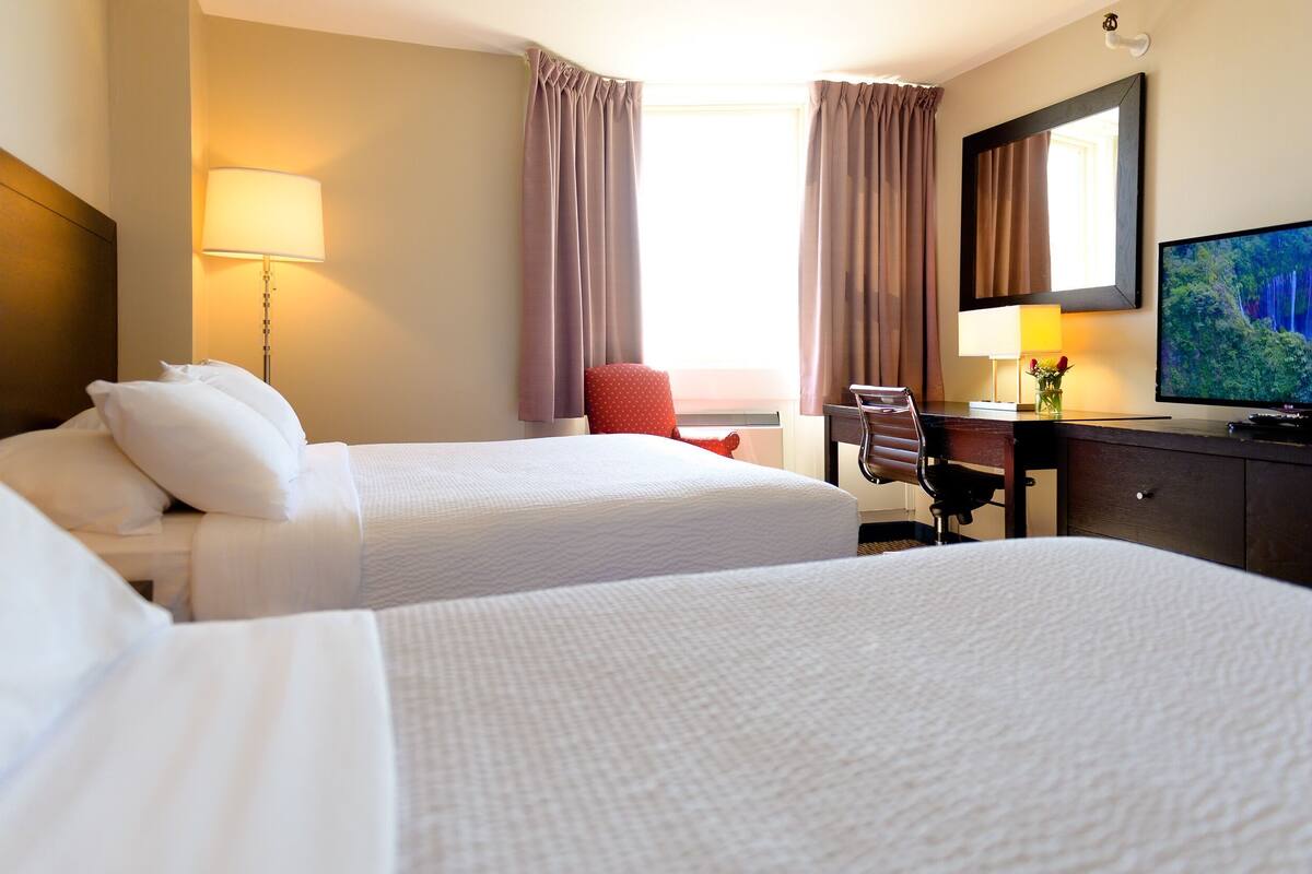 A hotel room with two beds, a desk, a chair, a television, and a lamp.
