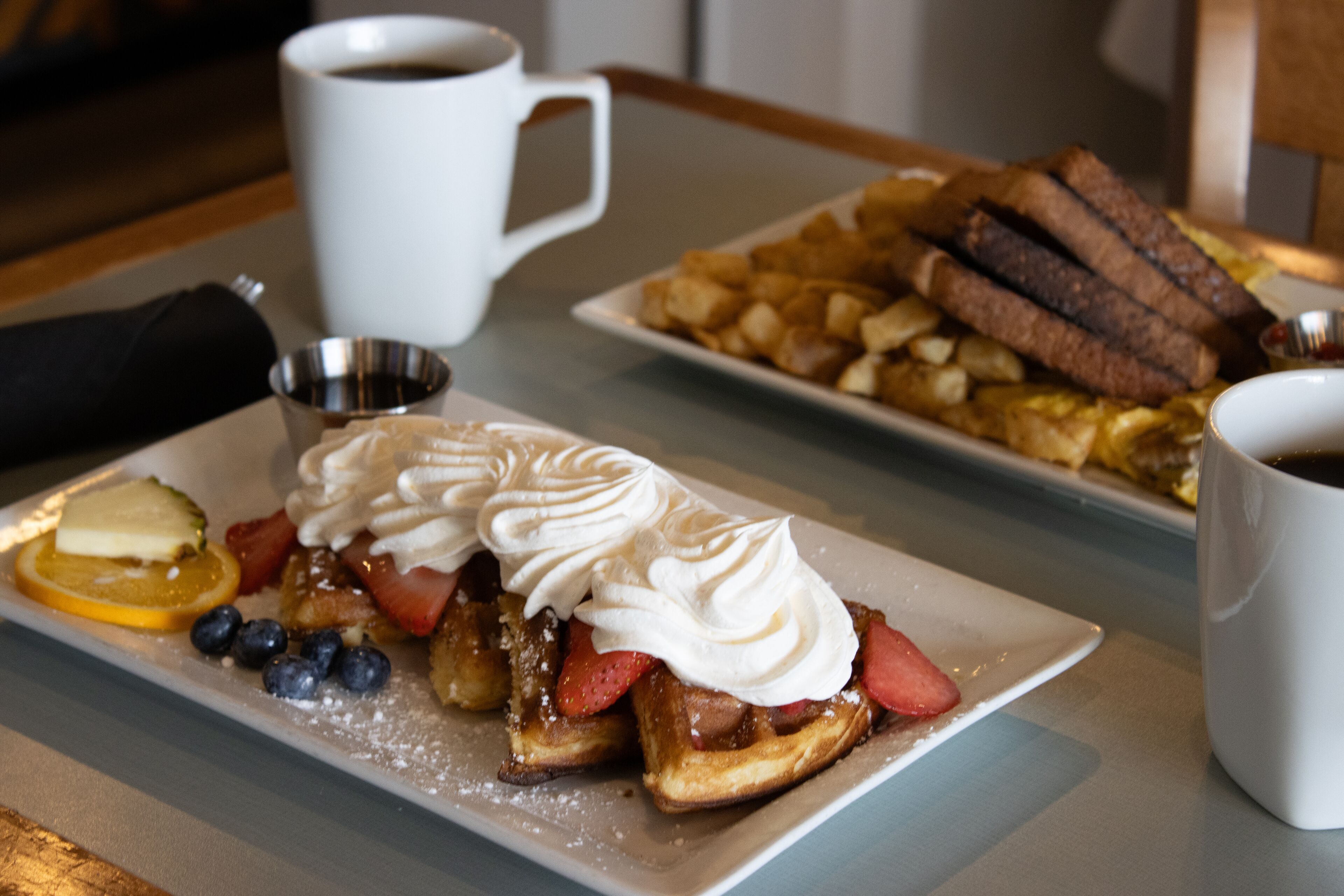 Un plato de desayuno con gofres, fresas, arándanos y crema batida.