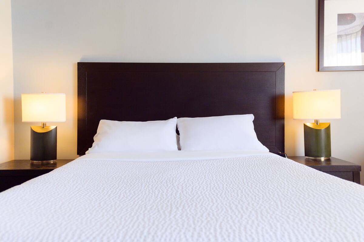 A neatly made bed with white linens, two bedside tables with lamps, and a dark headboard.