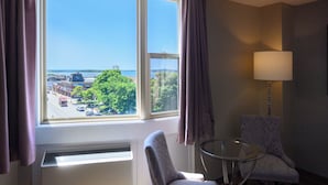 A hotel room with a large window, a chair, a table, and a lamp.