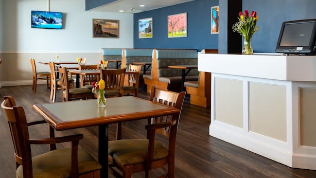 A restaurant interior with wooden tables and chairs, a reception desk, and wall-mounted artwork.