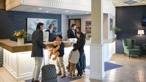 A hotel reception area with a reception desk, a large painting, and a green armchair.