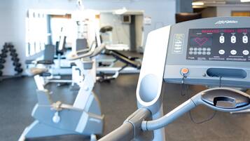 Una cinta de correr con pantalla digital que muestra frecuencia cardíaca y otras mediciones, en un gimnasio con diversos equipos de ejercicio.