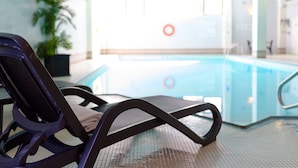 A pool area with a lounge chair and a pool with a lifeguard stand in the background.