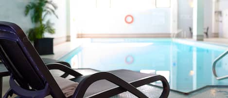 Un espace piscine avec des chaises longues et une piscine dont on aperçoit, au fond, le poste de surveillance du sauveteur.