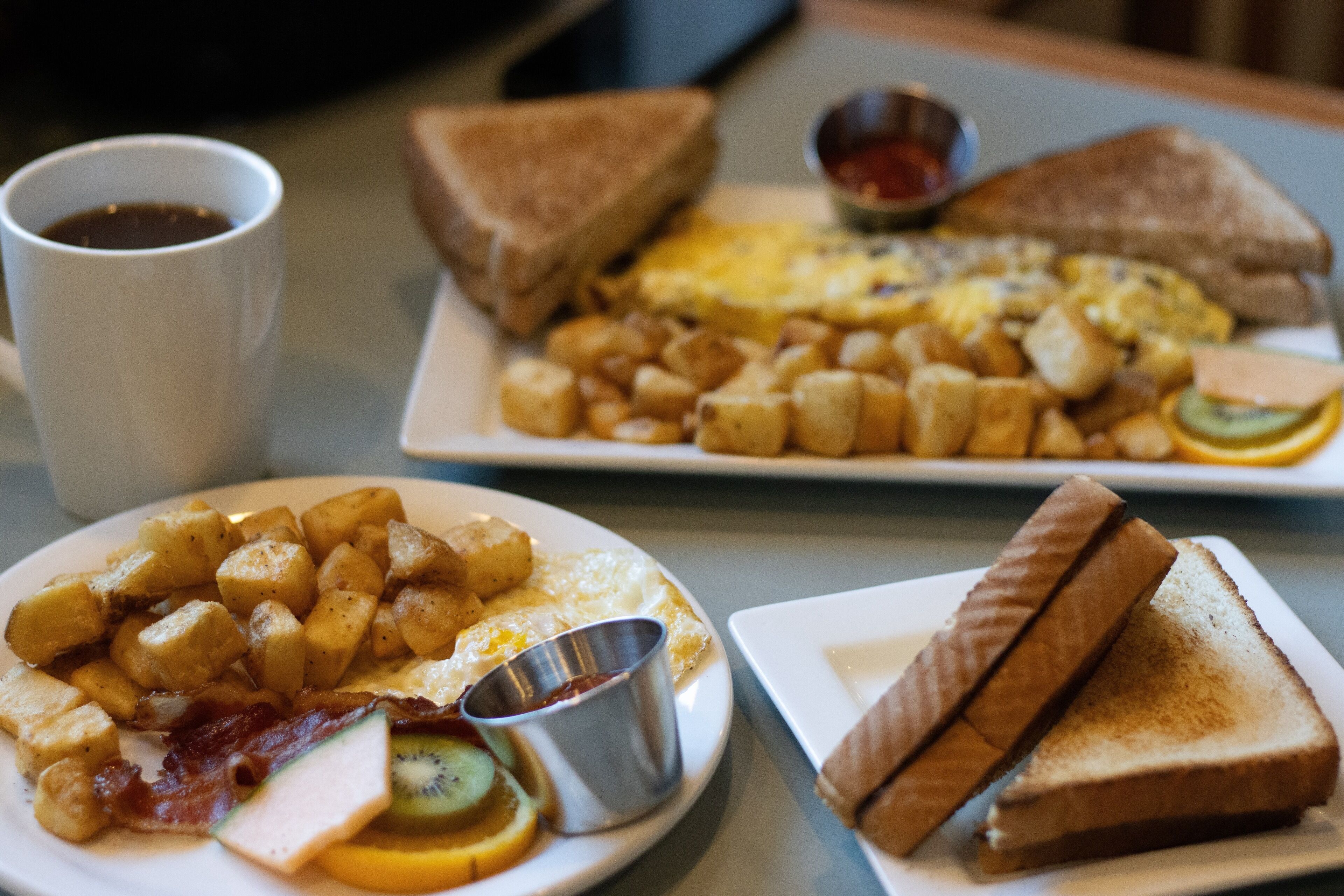 A breakfast plate with toast, eggs, potatoes, bacon, and a small cup of syrup.