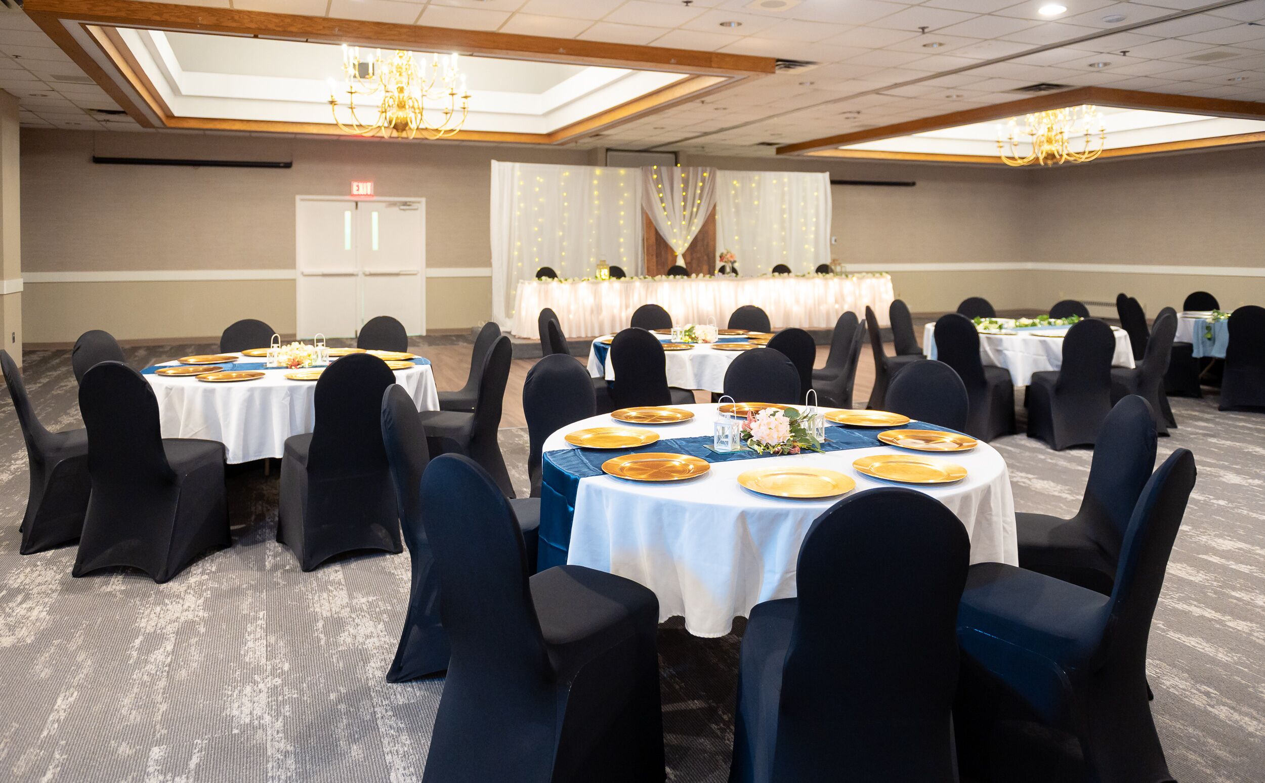 Une salle de banquet avec des tables rondes, des chaises noires et des nappes blanches.