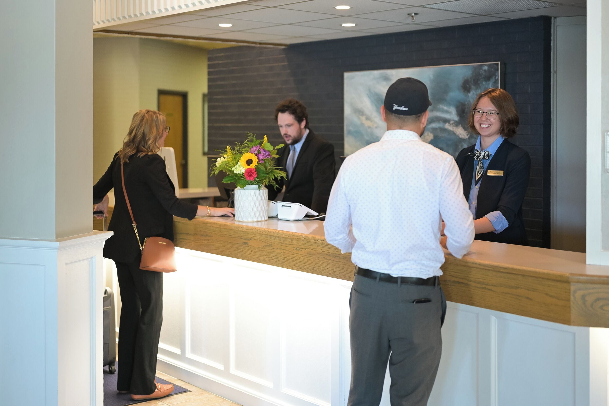 A reception area with a wooden counter, a vase with flowers, and a painting on the wall.