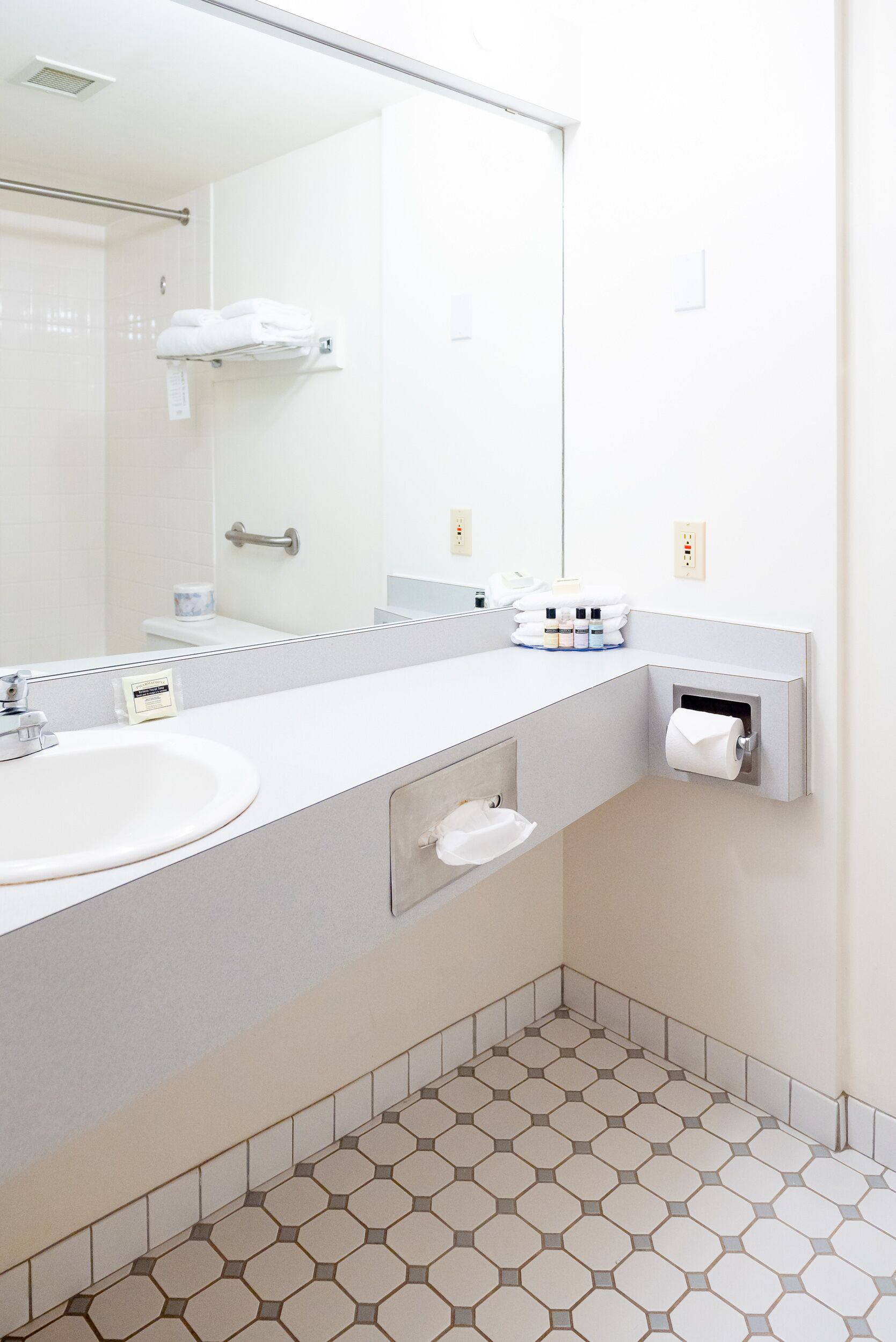 Ein modernes Badezimmer mit einem weißen Waschbecken, einem Spiegel, einem Handtuchhalter und einem Toilettenpapierrollenhalter.