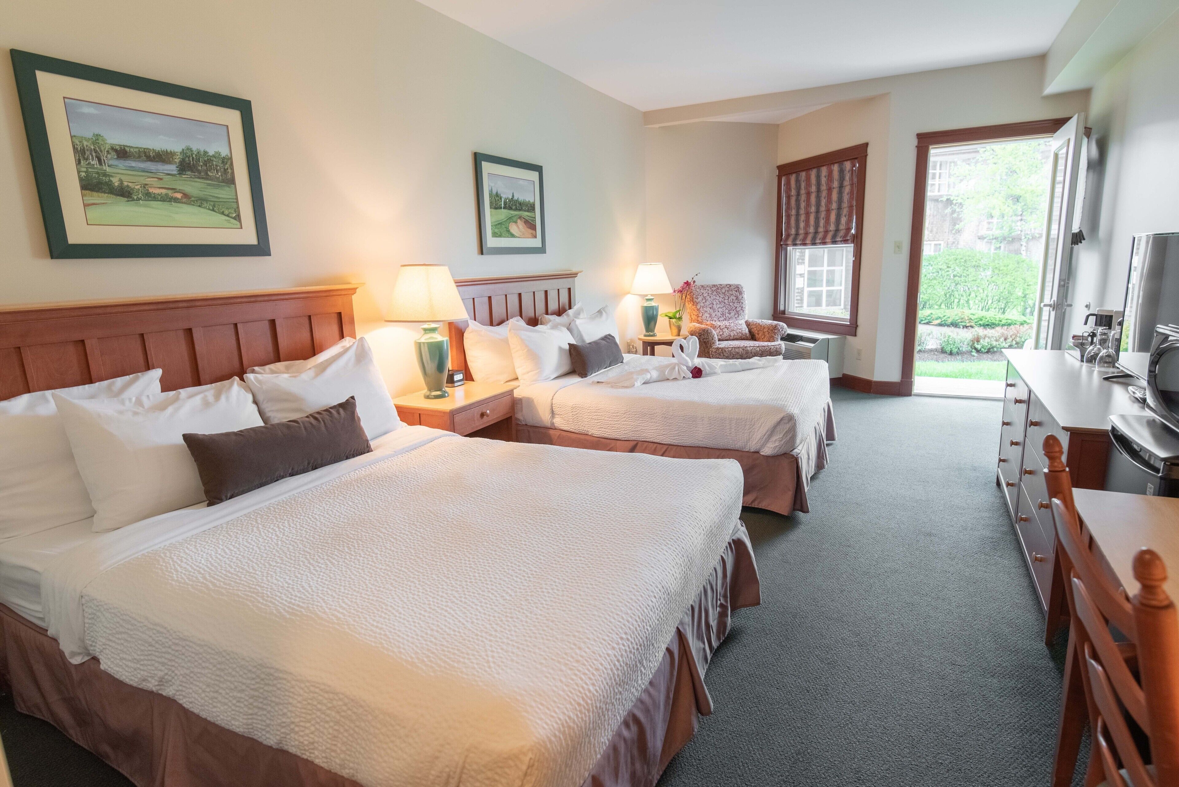 A hotel room with two beds, a desk, a chair, and a television.