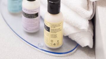 A bathroom with a white towel, a yellow soap bar, and three bottles of liquid soap.