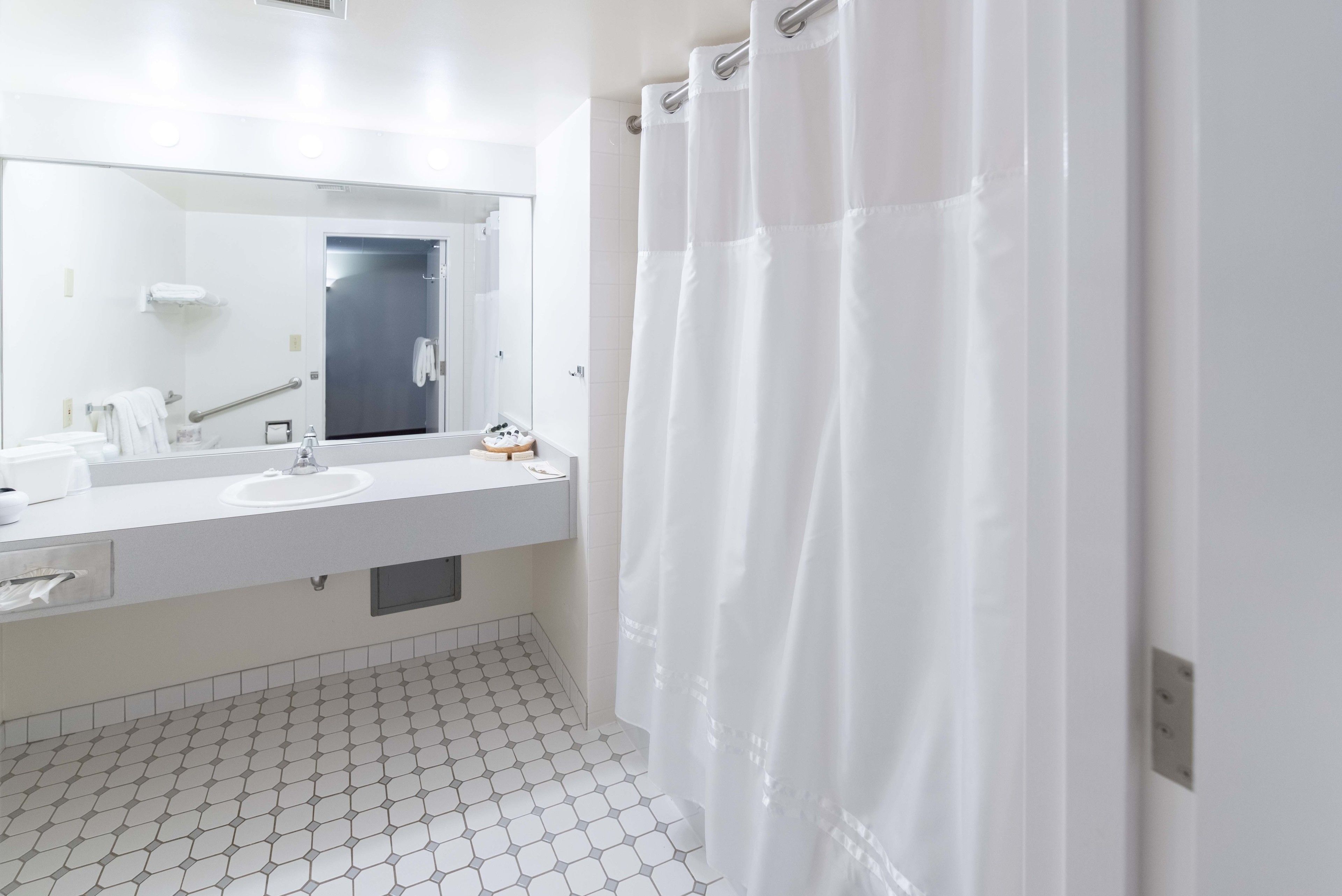 Une salle de bain moderne avec un lavabo blanc, un miroir et un rideau de douche.