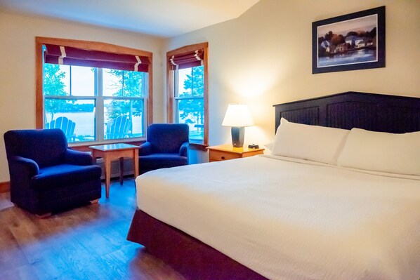 Une chambre d’hôtel avec un grand lit, deux fauteuils, une petite table et une lampe.