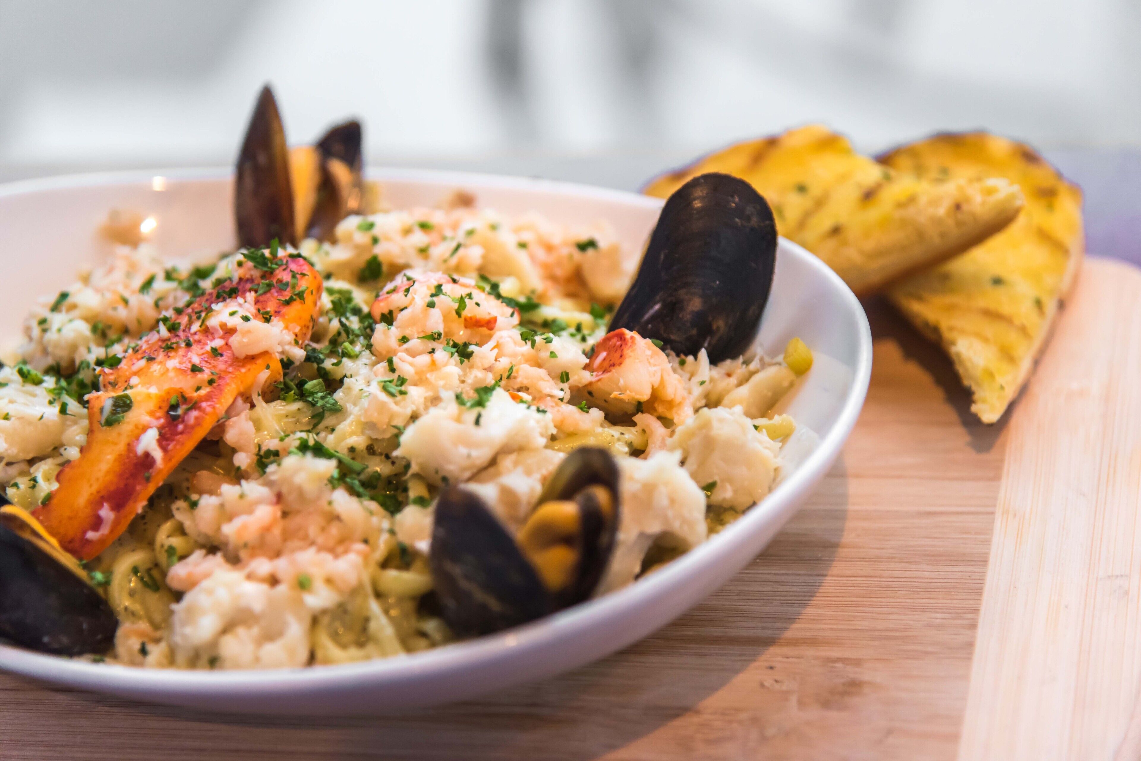 Un plato de mariscos con mejillones y camarones, adornado con hierbas, servido en un plato blanco con una mesa de madera al fondo.