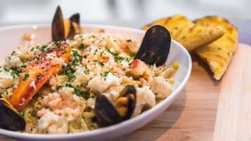 Un plato de mariscos con mejillones y camarones, adornado con hierbas, servido en un plato blanco con una mesa de madera al fondo.