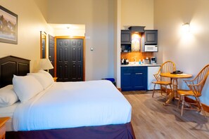 A hotel room with a bed, a desk, a chair, a microwave, and a sink.