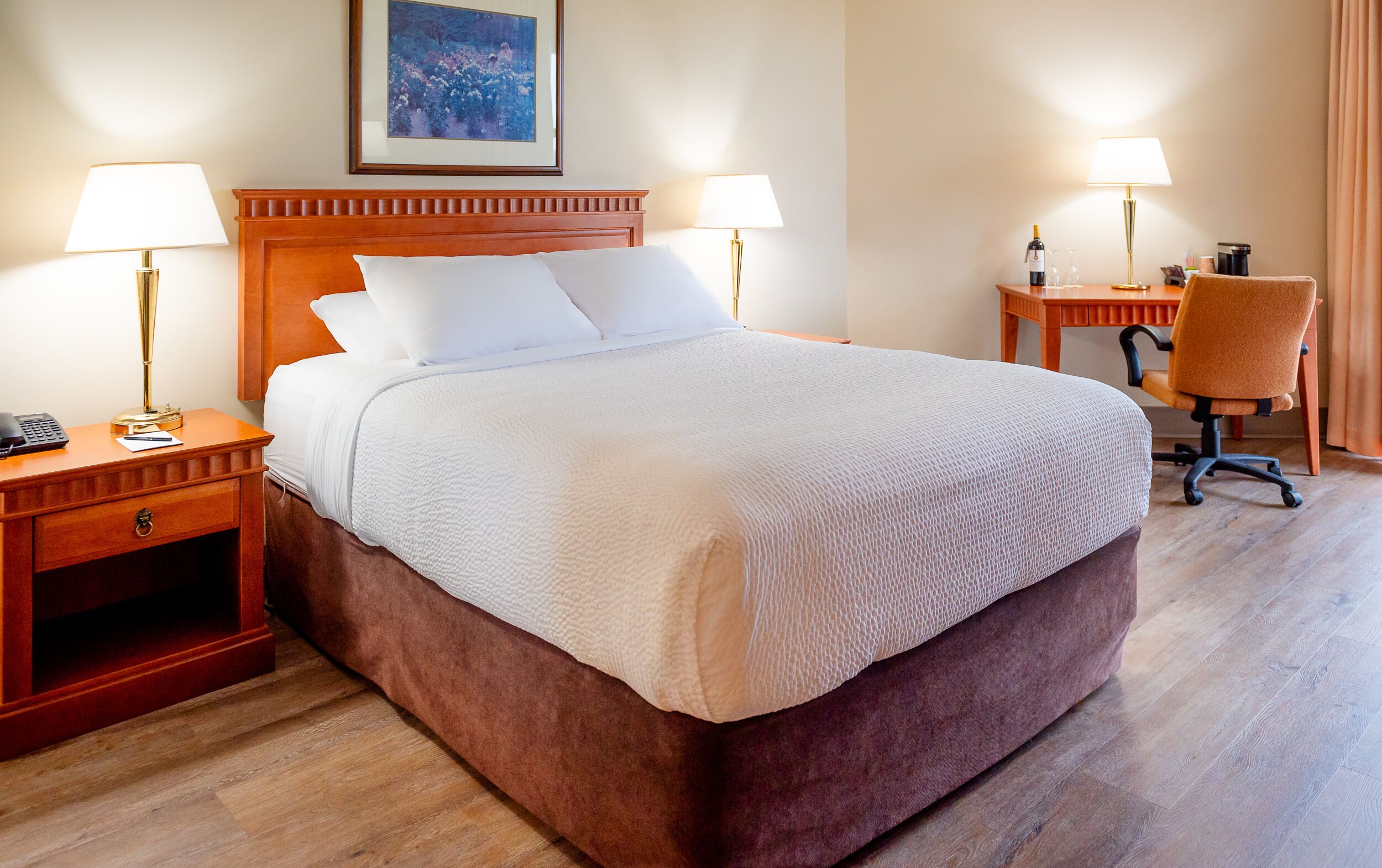 A hotel room with a large bed, two bedside tables with lamps, a desk with a chair, and a framed picture on the wall.