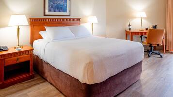 A hotel room with a large bed, two bedside tables with lamps, a desk with a chair, and a framed picture on the wall.