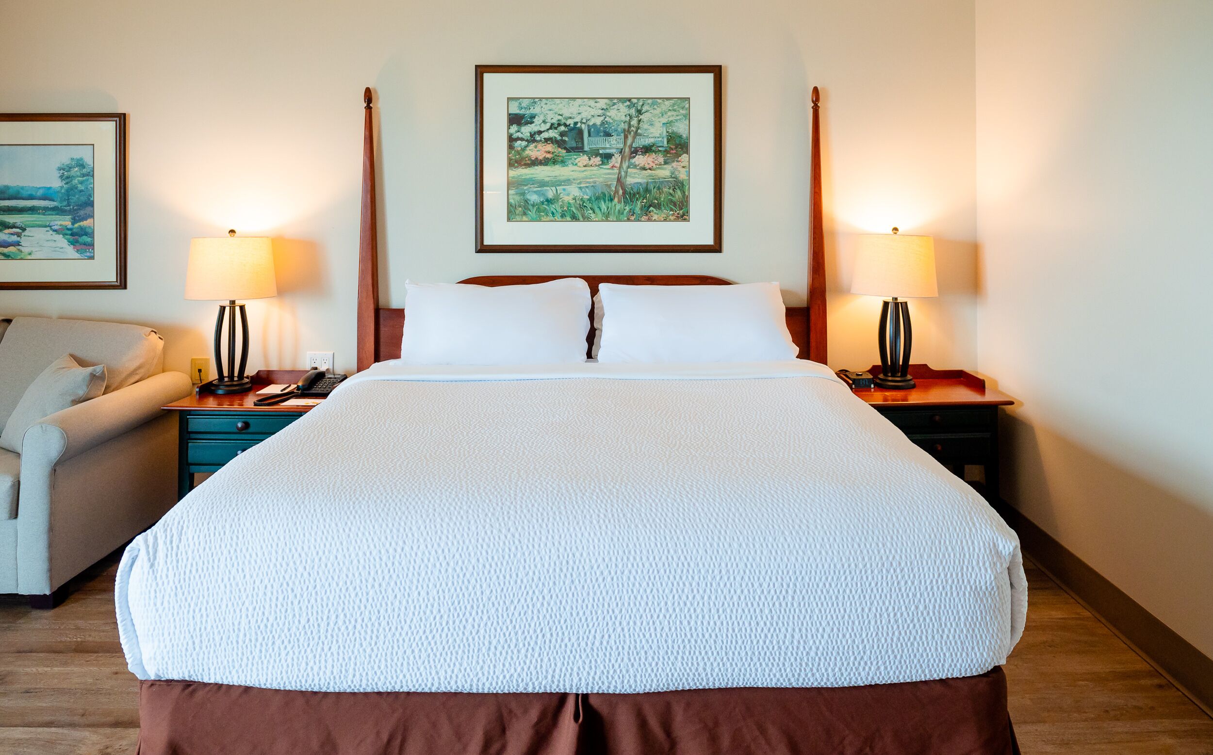 Habitación de hotel con una cama grande, dos mesitas de noche, una silla y cuadros en las paredes.