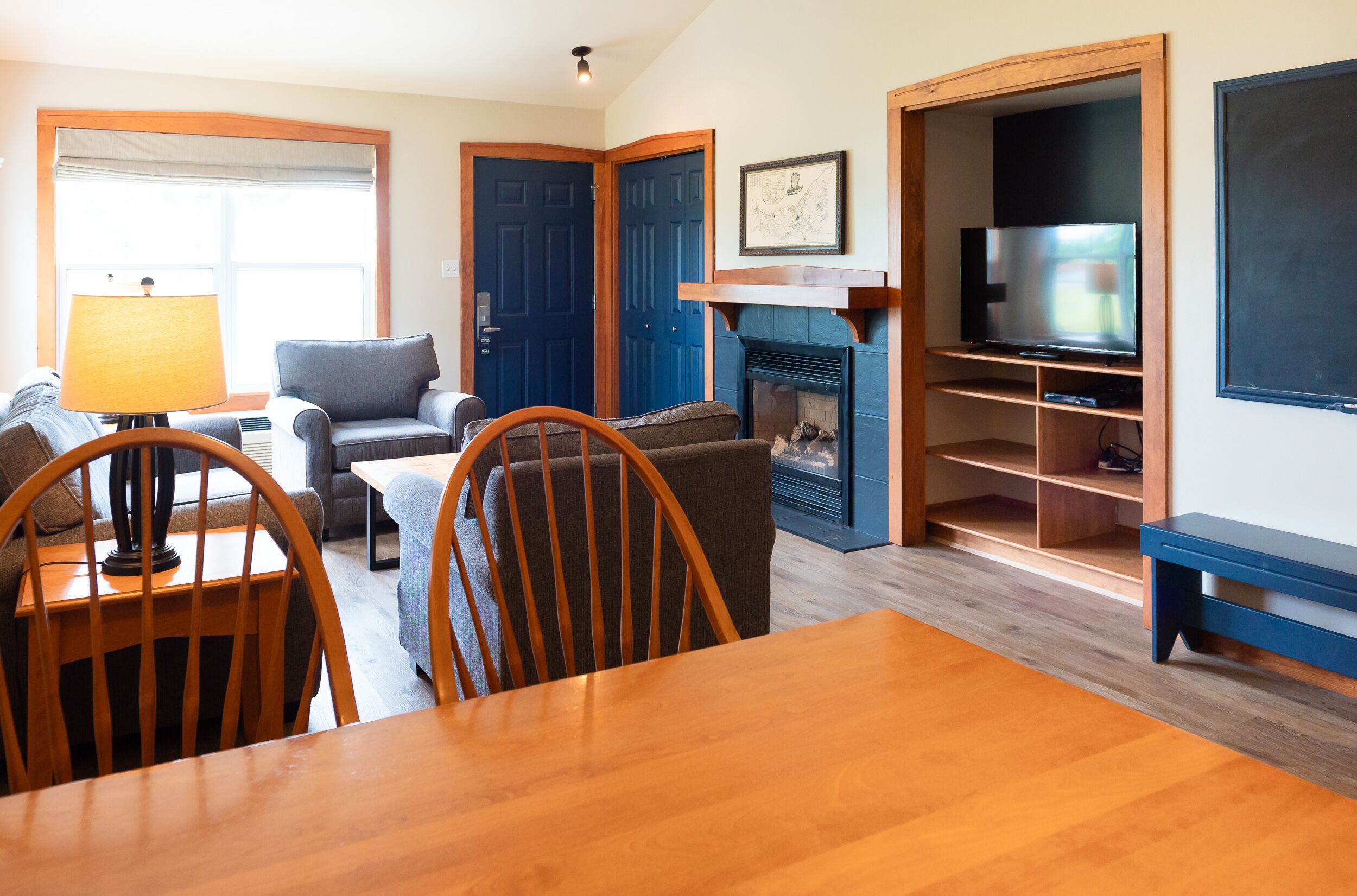 A living room with a wooden dining table, two wooden chairs, a sofa, a lamp, and a fireplace.