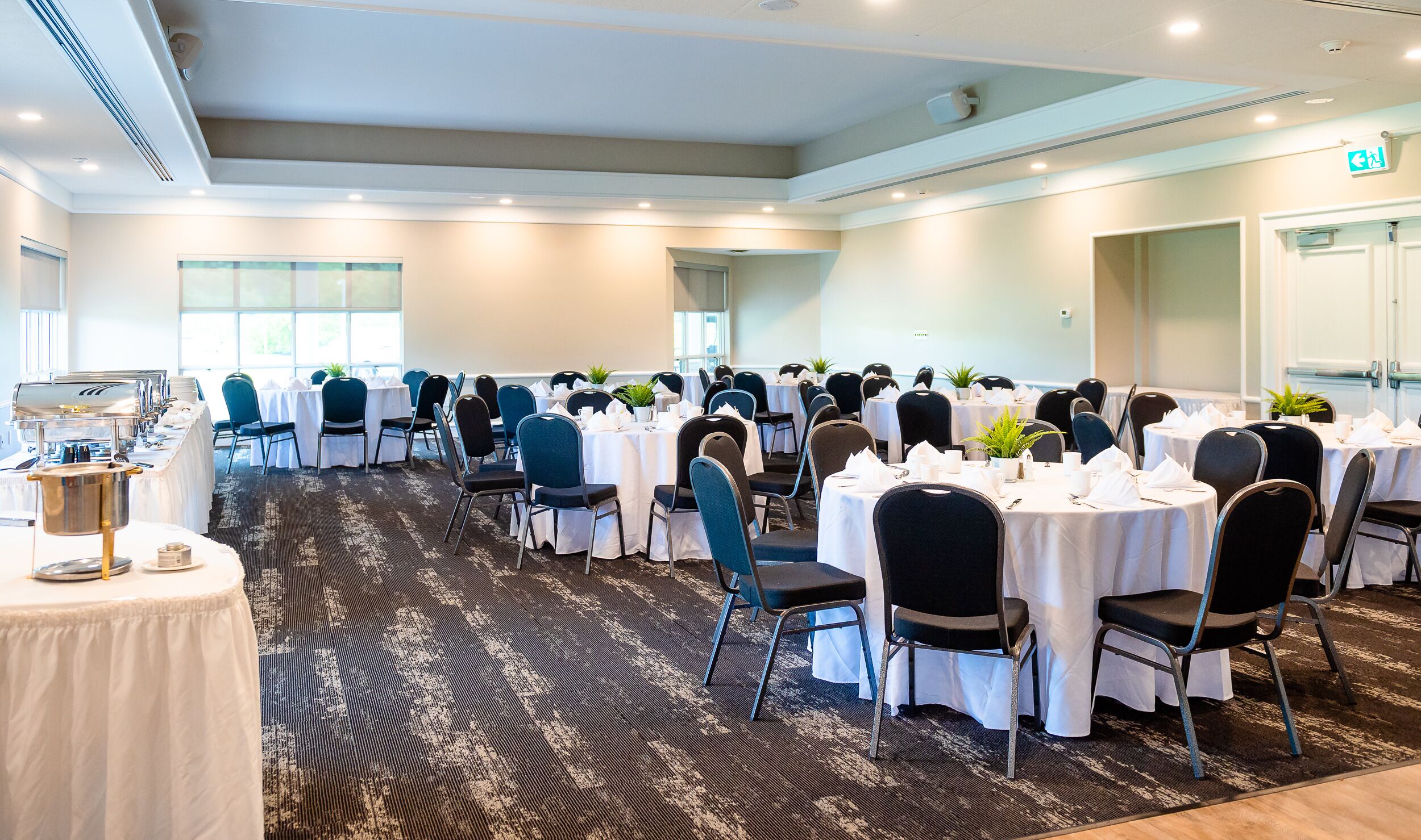 Salón de conferencias con mesas redondas, sillas y un montaje tipo buffet.