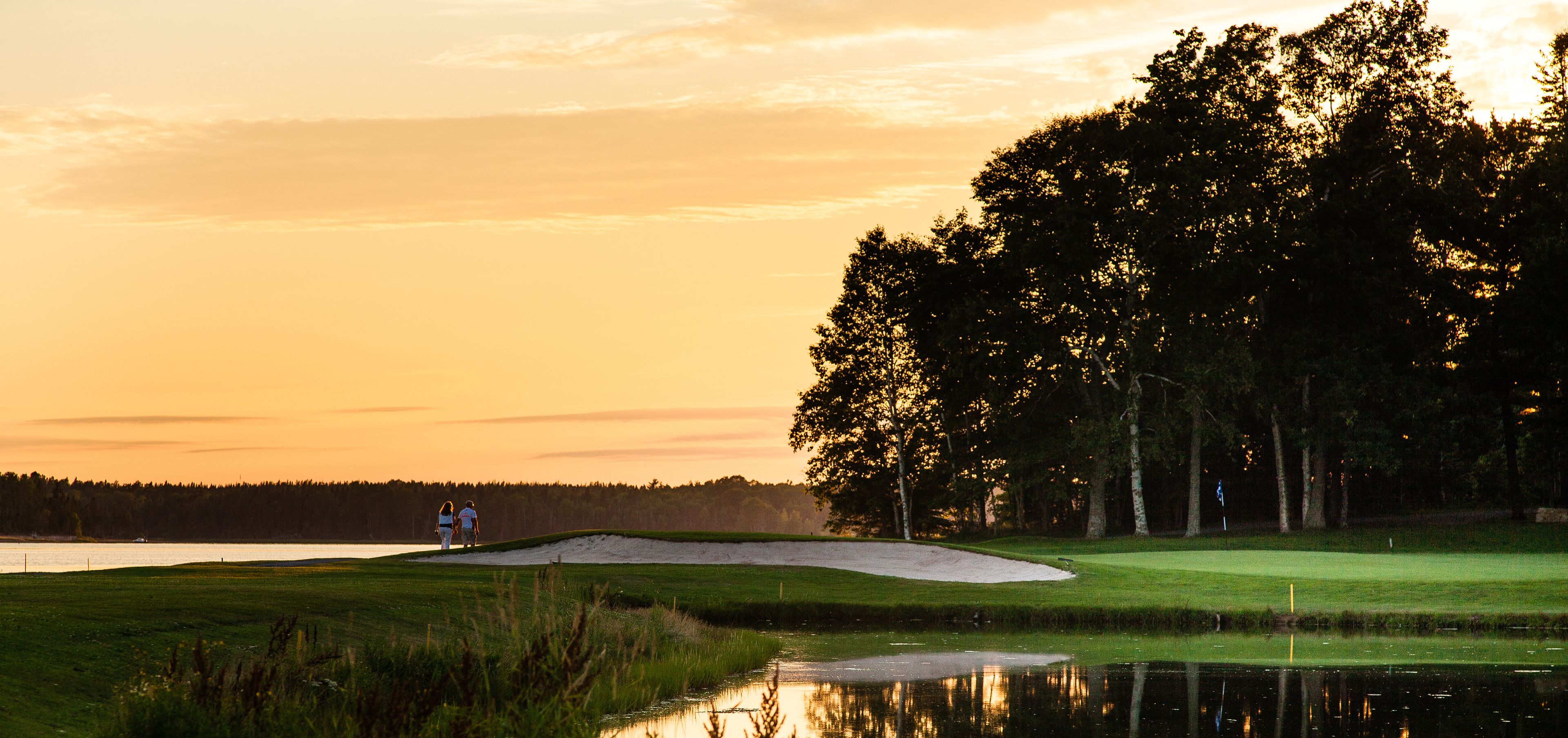 Un parcours de golf avec un plan d’eau qui reflète le ciel, entouré d’arbres et offrant une vue dégagée sur l’horizon.
