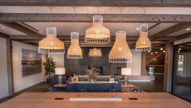 Un comedor amplio con una larga mesa de madera y sillas modernas, rodeado de lámparas colgantes de mimbre.