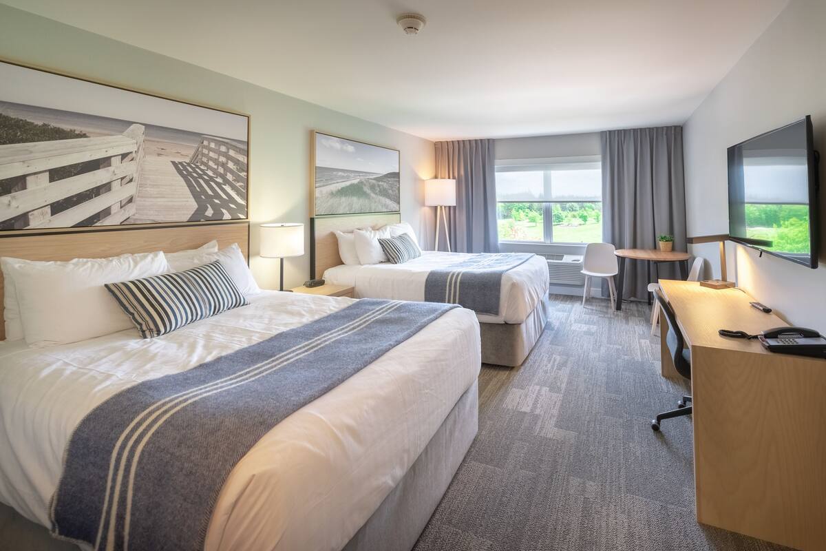 Une chambre d’hôtel avec deux lits, un bureau, une chaise et une télévision.