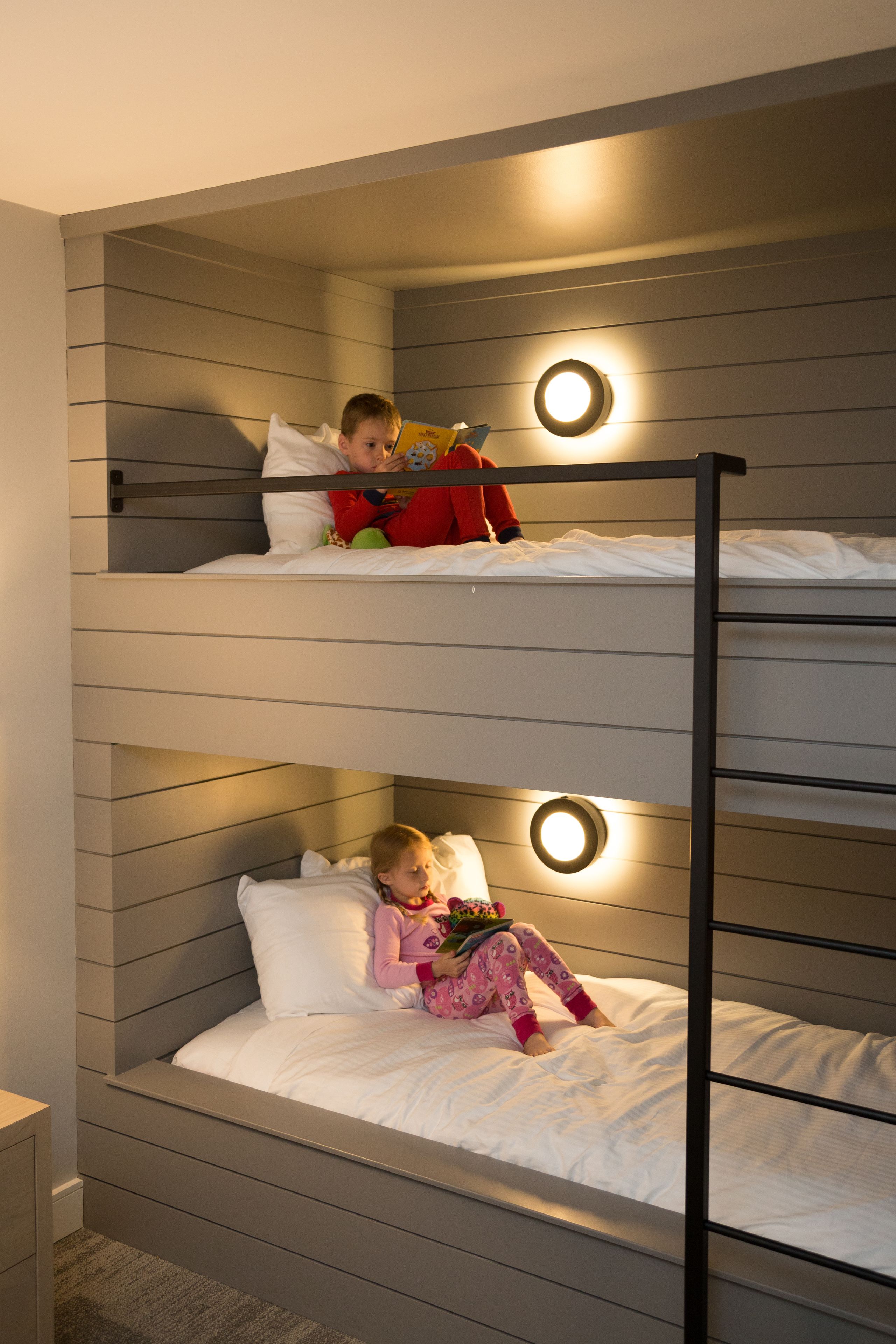 Un lit superposé à deux niveaux, chaque niveau étant équipé d’un luminaire circulaire.
