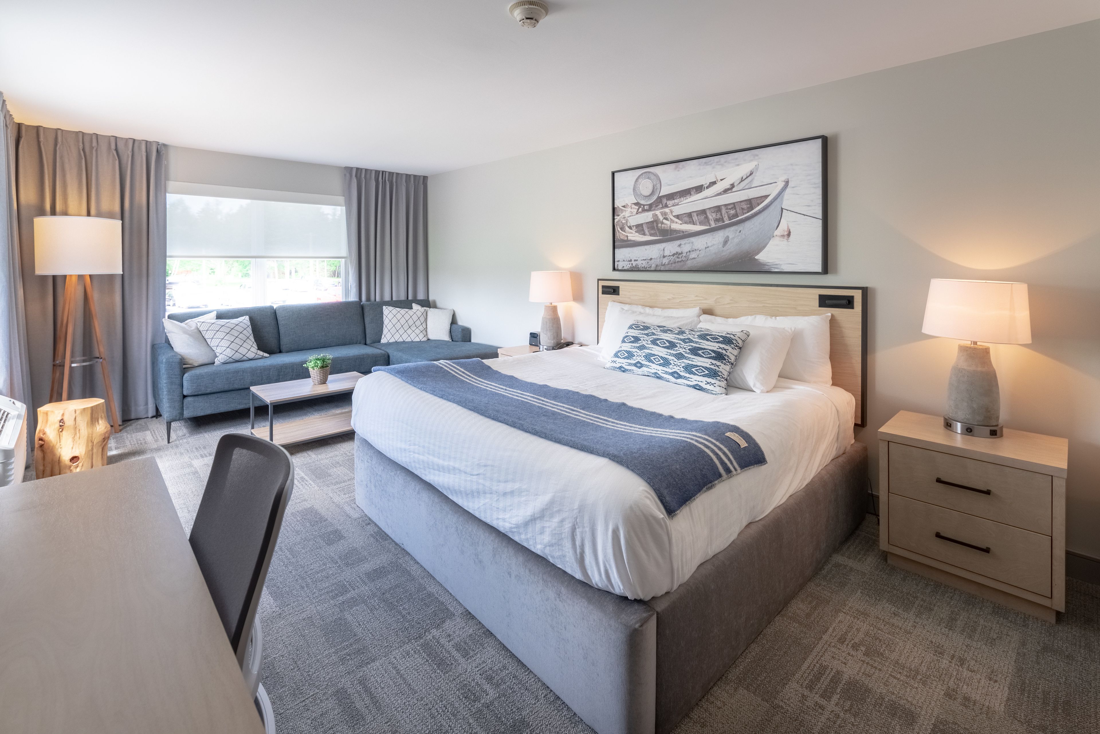 A modern hotel room with a large bed, a sofa, a desk, and a window with curtains.