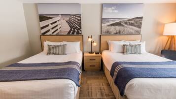Una habitación de hotel con dos camas, cada una con cabecero de madera, una mesita de noche entre ellas y una lámpara a la derecha.