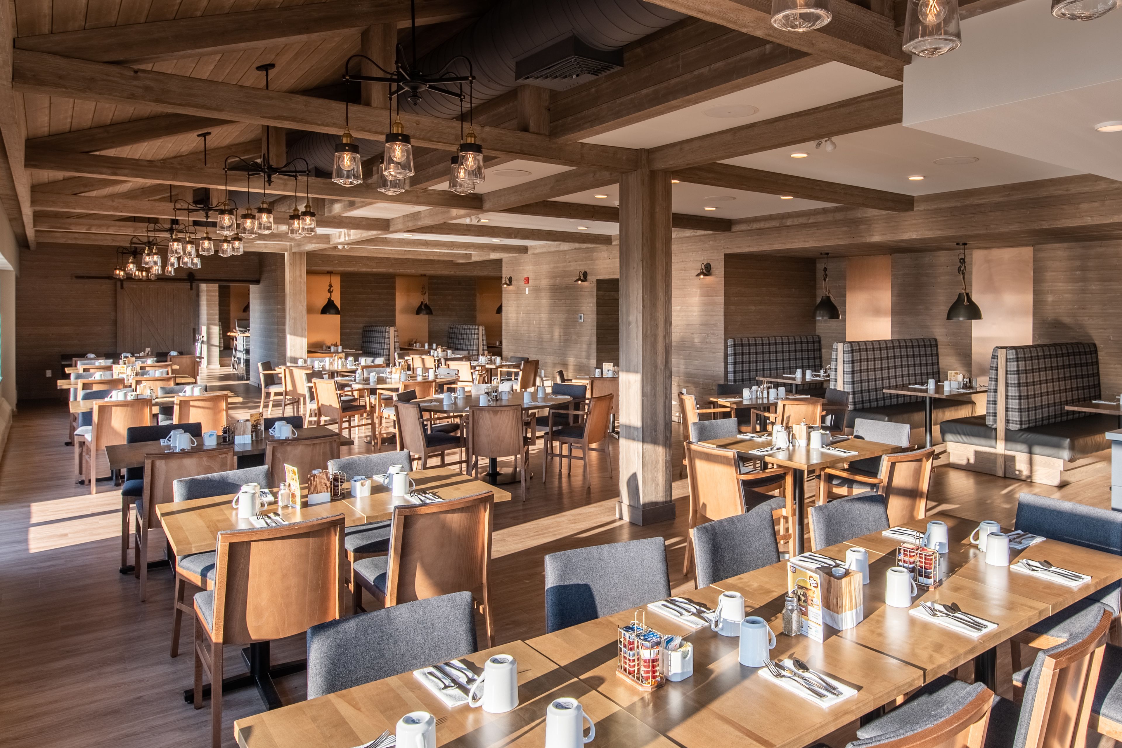 A spacious dining area with wooden tables and chairs, modern pendant lighting, and a cozy ambiance.