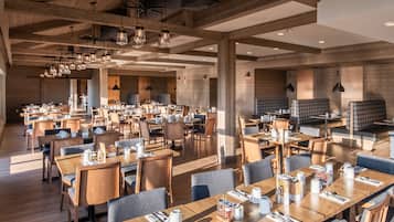 A spacious dining area with wooden tables and chairs, modern pendant lighting, and a cozy ambiance.