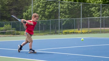 A tennis court with a player in a red shirt and beige shorts.