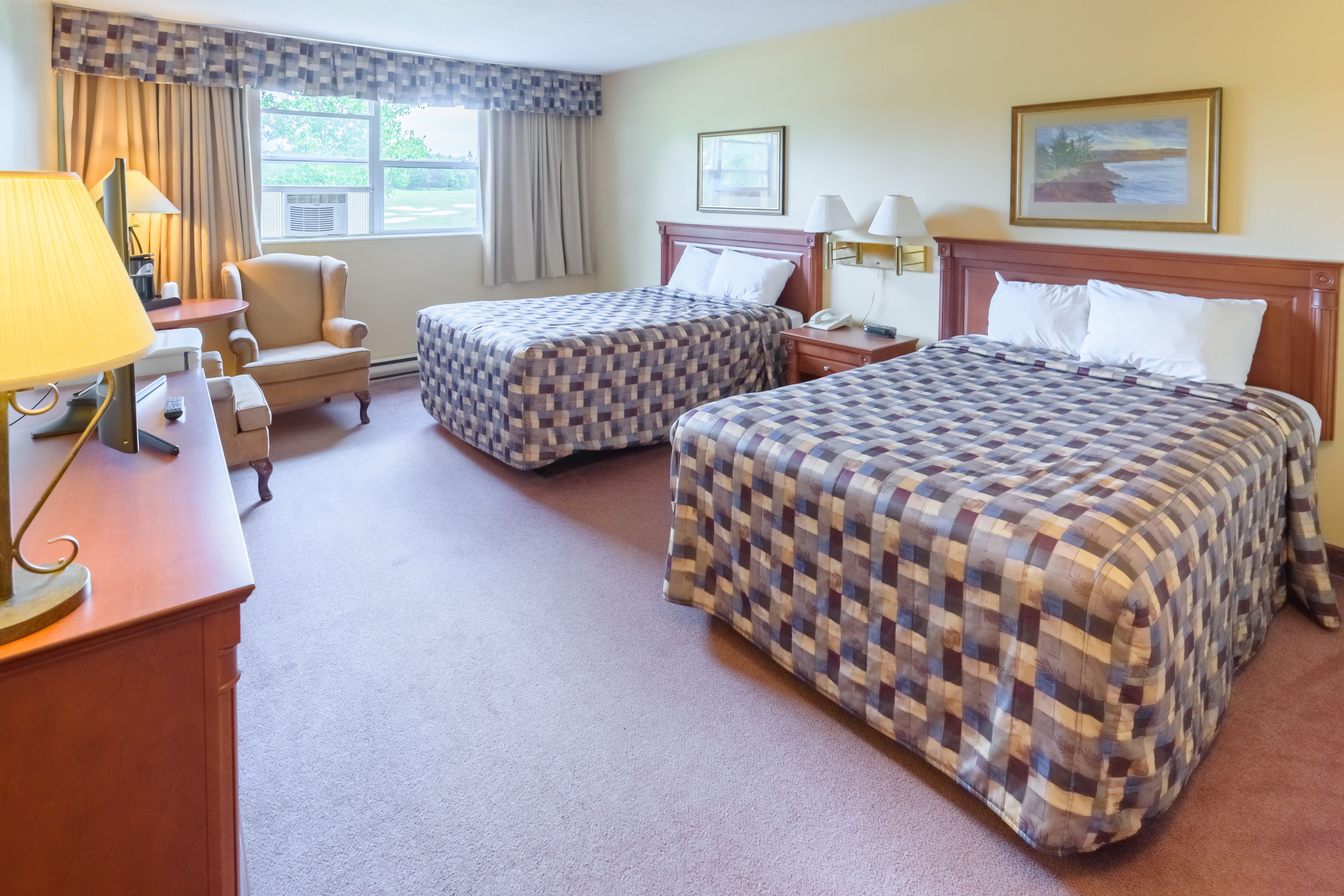 A hotel room with two beds, a desk with a lamp, a chair, and a window with curtains.