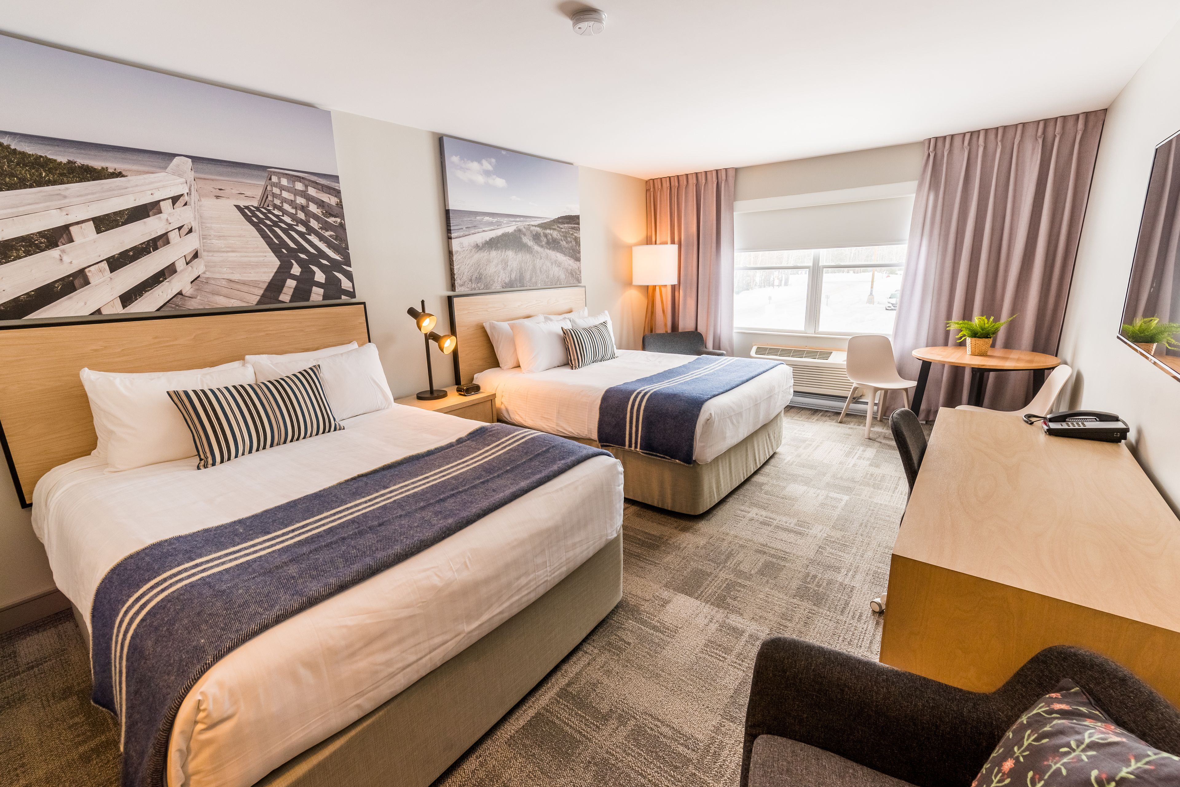 A hotel room with two beds, a desk, a chair, and a large window.