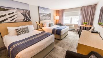 A hotel room with two beds, a desk, a chair, and a large window.