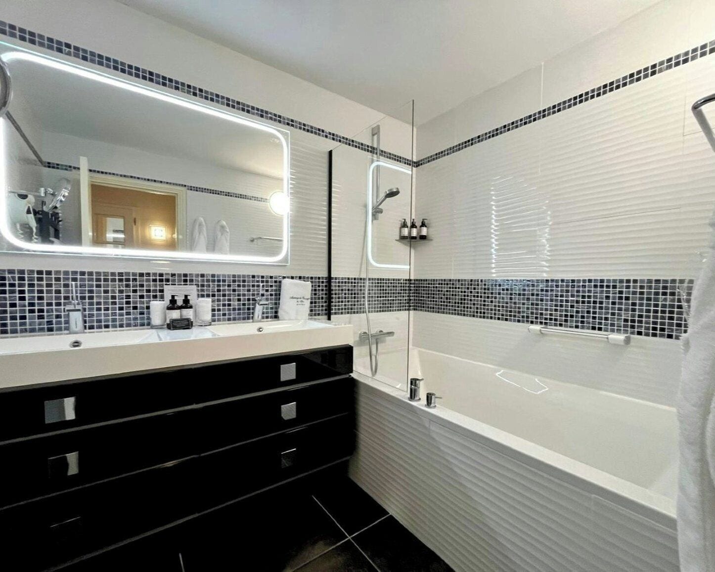 Ein modernes Badezimmer mit einem großen Spiegel, einer Badewanne und einem Waschtisch mit einem schwarzen Schrank.