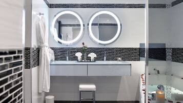 A modern bathroom with two round mirrors, a white sink, and a small stool.