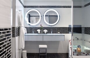 A modern bathroom with two round mirrors, a white sink, and a small stool.