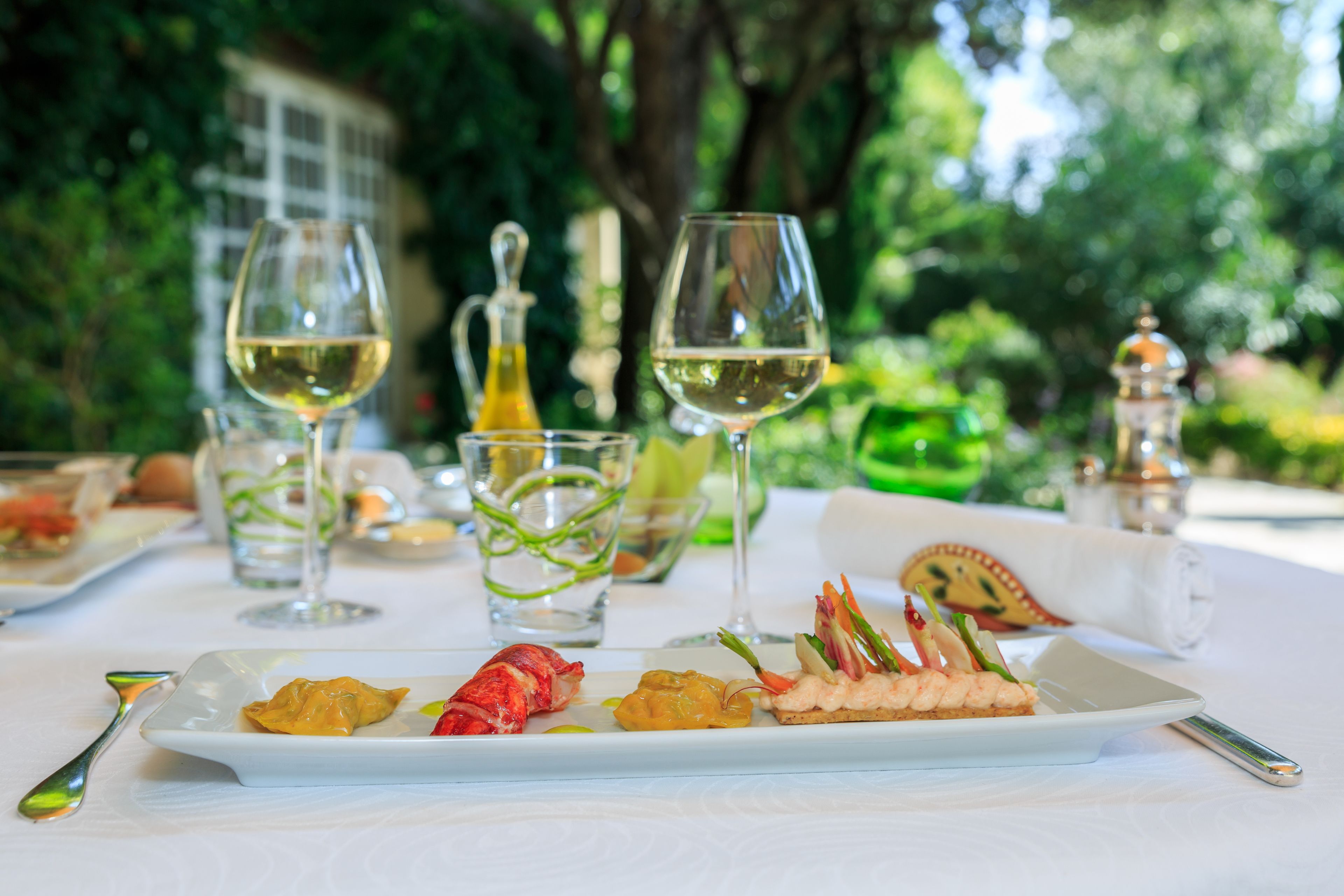A dining table with a white tablecloth, plates of food, and two wine glasses.