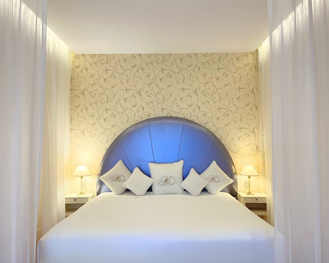 A hotel room with a large bed, a decorative headboard, and two bedside tables with lamps.