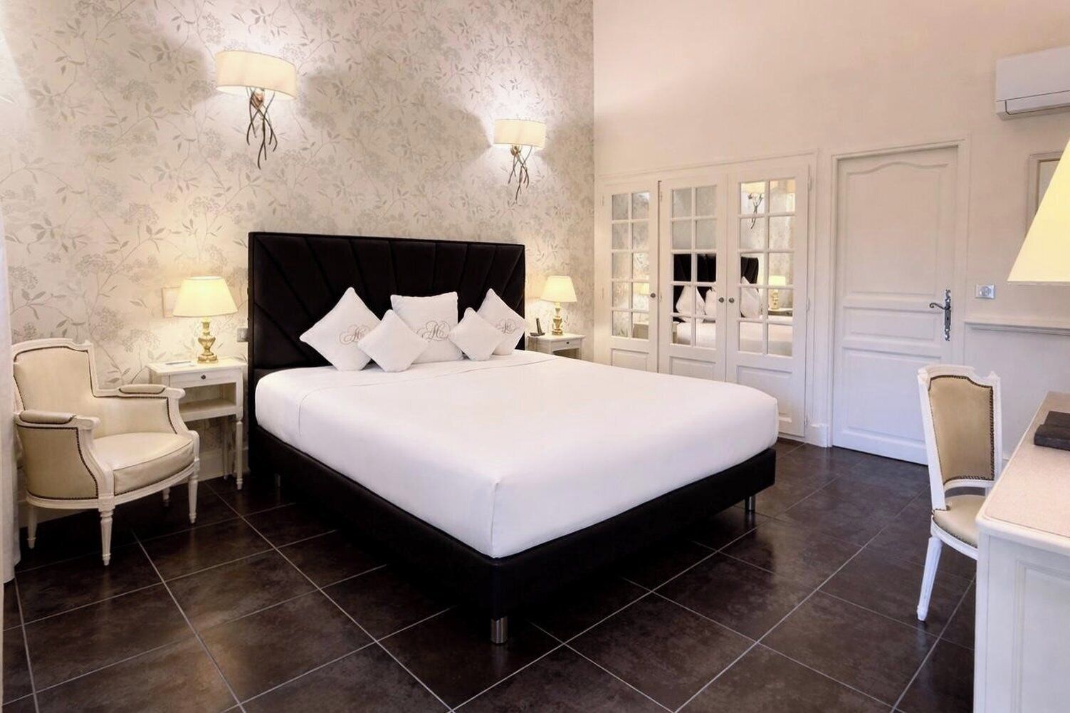 A hotel room with a large bed, two bedside tables with lamps, a chair, a desk, and a wardrobe with glass doors.