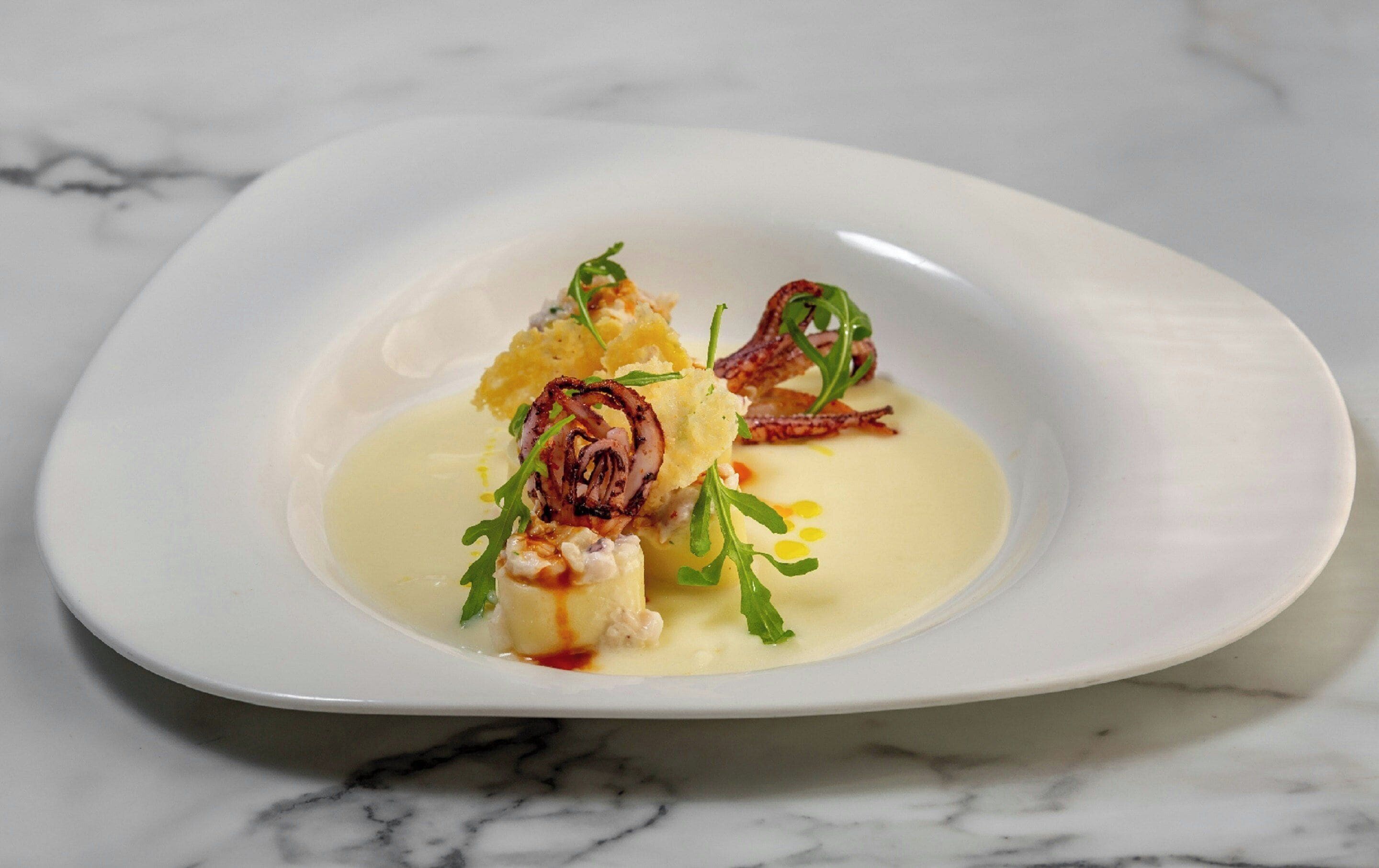 Une assiette blanche contenant un plat, agrémenté de verdure et d’une sauce.