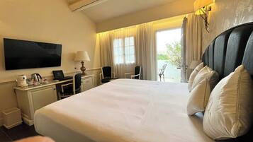 A hotel room with a large bed, a desk with a lamp, a chair, and a TV.