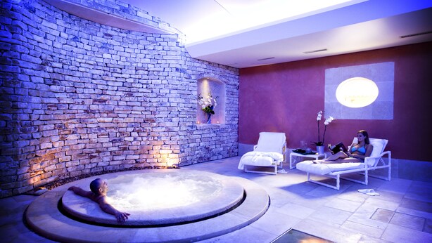 Un área de spa con pared de piedra, un jacuzzi y dos sillones de relax.
